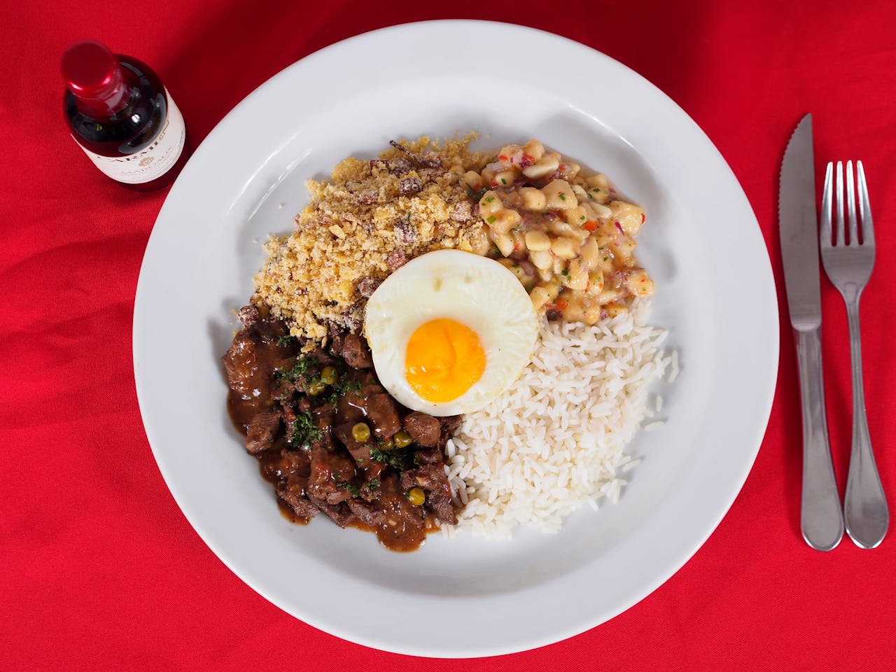 Home A vibrant Brazilian Feijoada meal with rice, beans, and a fried egg on a red background.